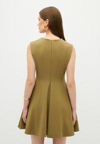Ärmelloses, olivgrünes Kleid mit tailliertem Oberteil, ausgestelltem Rock und Rückenreißverschluss. Glattes Gewebe mit einem klaren, minimalistischen Design.