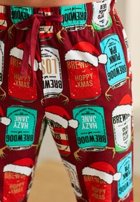 Red pajama pants featuring colorful beer can graphics with Santa hats, a drawstring waistband, and a soft, smooth texture.