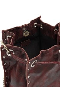 Burgundowa skórzana torebka o teksturowanym wykończeniu, z otwartą górą i srebrnymi akcentami, z oczkami oraz zapięciem na zatrzask w środku.