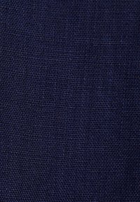 Gros plan d’un tissu bleu foncé tissé serré avec un motif texturé en forme de grille et des fils légèrement surélevés.