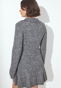 Sivý pletený sveter šaty s dlhými rukávmi, priliehavým telom a rozšíreným lemom, s textúrovanou tkaninou a detailom goliera.
