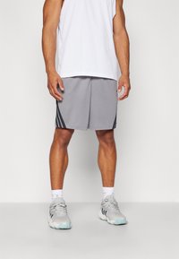 Szürke sportnadrág fekete oldalsávokkal, fehér hálós ujjatlan pólóval és szürke sneakers cipővel párosítva. A nadrág laza szabású és sima tapintású.