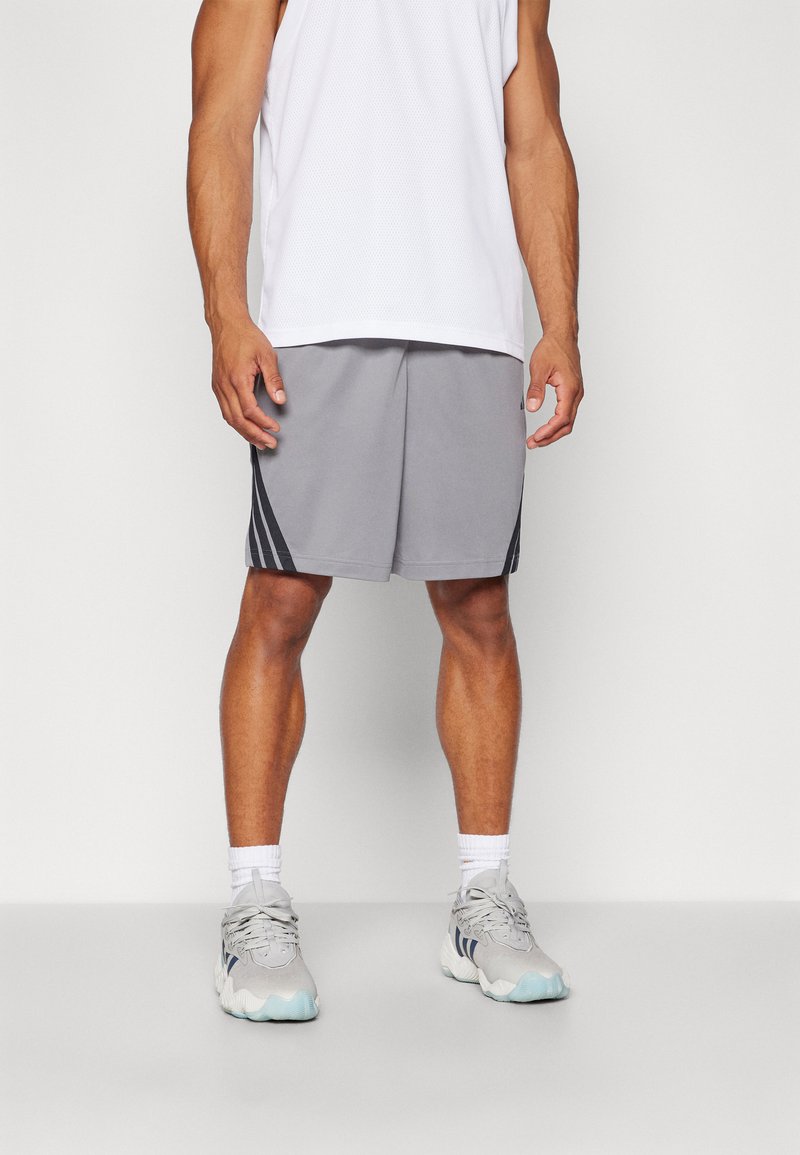 Szürke sportnadrág fekete oldalsávokkal, fehér hálós ujjatlan pólóval és szürke sneakers cipővel párosítva. A nadrág laza szabású és sima tapintású.