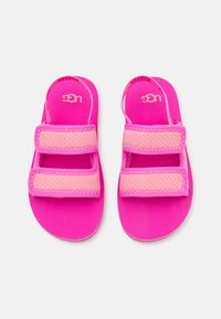 Roza sandali z dvema širokima Velcro trakoma, ki imajo teksturirano zasnovo. Gladek podplat z logotipom UGG v kontrastni barvi.
