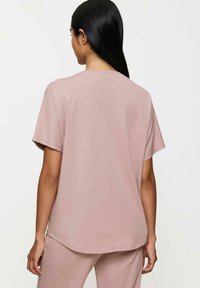 Jasnoróżowa koszulka z krótkim rękawem o luźnym fasonie, okrągłym dekolcie i gładkiej fakturze, z centralnym szwem na plecach.