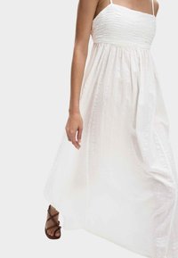 Witte maxi-jurk met een gewatteerd, geplooid lijfje, dunne bandjes en een vloeiende rok. Draagt het met bruine sandalen met bandjes voor contrast.