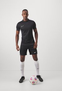 Schwarzes Nike Kurzarm-Trikot mit weißen Akzenten, schwarze Shorts, weiße Socken und schwarze Fußballschuhe, stehend mit einem mehrfarbigen Fußball.