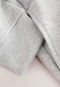 Tessuto di felpa grigio con una trama liscia e polsini a costine. Strati sovrapposti mostrano una combinazione di superficie morbida e motivi sottili.