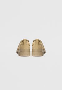 Adidași din suede bej cu o talpă groasă din cauciuc. Au un tab de călcâi cu buclă și un logo embossat în partea din spate. Design minimalist.