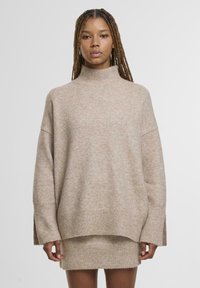 Beige, oversize pulóver magas, álló nyakkal, széles ujjal és bordázott aljjal. Puha tapintású, finom melírozott mintázattal.