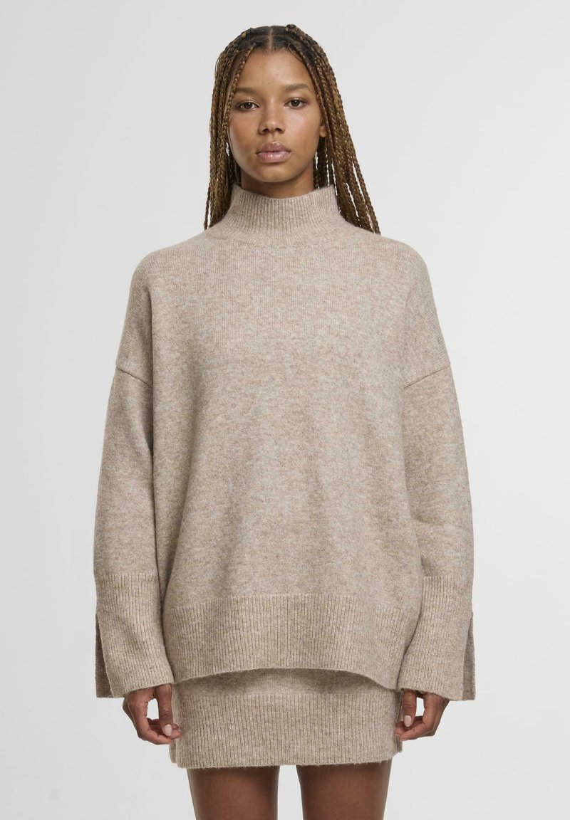 Beige, oversize pulóver magas, álló nyakkal, széles ujjal és bordázott aljjal. Puha tapintású, finom melírozott mintázattal.