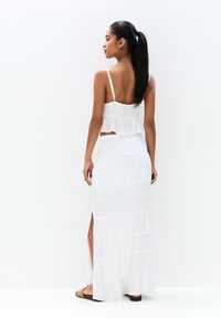Robe blanche avec une texture en couches et volants, bretelles spaghetti ajustables et une fente latérale. Associée à des sandales plates au design minimal.
