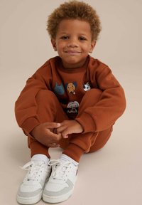 Completo di felpa e pantaloni marroni con cani dei cartoni animati sul davanti, abbinato a sneakers bianche e calzini bianchi alla caviglia.