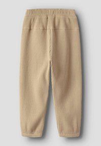 Beige ribbestrikkede bukser med elastisk midje, med smale ben og teksturert overflate, vist bakfra.