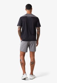 Czarny i szary sportowy T-shirt z krótkimi rękawami i prążkową teksturą, zestawiony z szarymi szortami. Model ma widoczne tatuaże na nogach.