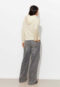 Haut à capuche beige avec une finition texturée et un cordon de serrage, associé à un jean en denim gris à jambes larges avec des poches arrière.