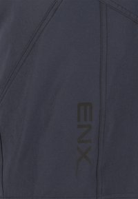 Laivastonsininen kangas, jossa on voimakkaat ompeleet ja sileä pinta, sekä musta logo, joka on painettu pystysuoraan kylkeen.