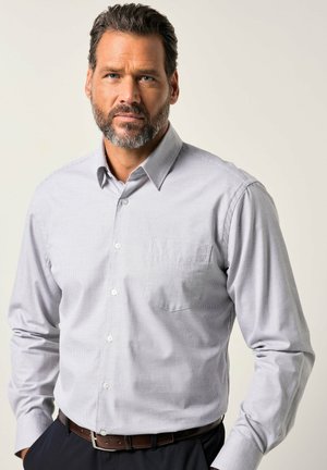 Camisa de botones a cuadros en gris claro, con un bolsillo, mangas largas y cuello estructurado. Combinada con un cinturón marrón oscuro de textura sutil.