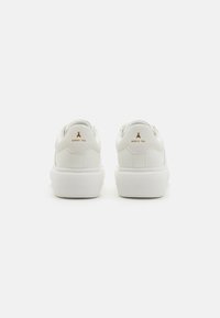Hvite skinnsneakers med glatt finish, med en teksturert hvit gummisåle og en liten gull-logo på hælen.