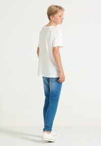 Witte T-shirt met korte mouwen en een ronde hals, gecombineerd met lichtblauwe slim-fit jeans en witte sneakers. Eenvoudig ontwerp, minimale details.