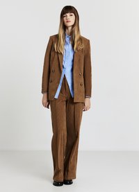 Brauner Cord-Anzug mit einem doppelreihigen Blazer und gerade geschnittenen Hosen, kombiniert mit einem hellblauen Hemd mit Knöpfen.