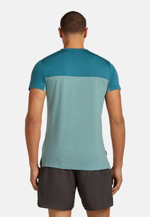 T-shirt à manches courtes avec un design bicolore en bleu clair et turquoise, fabriqué en tissu doux et texturé. Finitions comprenant un col rond et des fentes sur les côtés.