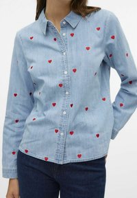 Camicia in denim blu chiaro con cuori rossi ricamati sparsi sul tessuto, dotata di colletto e chiusura con bottoni.