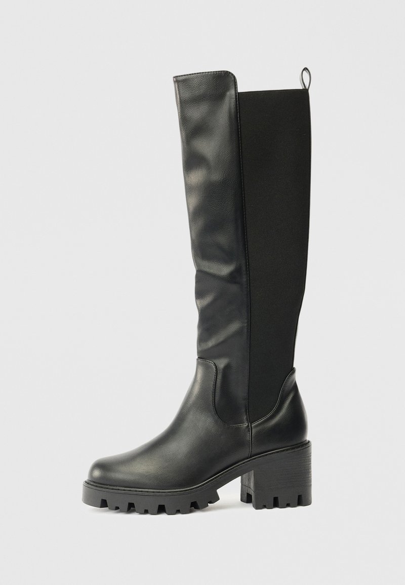 Botas negras hasta la rodilla con una combinación de cuero suave y tela texturizada, que presentan una suela gruesa y un tacón cuadrado para mayor estabilidad y agarre.