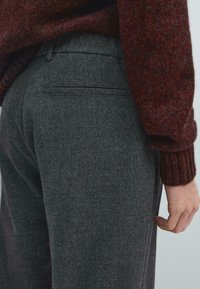 Pantaloni grigi scuri su misura con un sottile motivo testurizzato, dotati di una tasca posteriore e una vestibilità slim, abbinati a un maglione testurizzato color bordeaux.