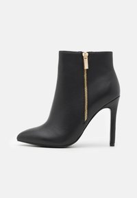 Bota de cuero negro hasta el tobillo con puntera afilada, tacón de aguja alto y cremallera lateral con herrajes dorados. Textura suave, diseño elegante.