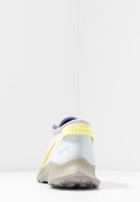 Chaussure de course Nike Trail Pegasus avec une tige bleu clair, des accents jaunes, et une semelle grise texturée conçue pour la traction et le confort.