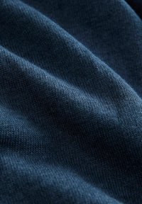 Tmavomodrá pletená tkanina s jemnou textúrou, ktorá vysoko kvalitne pôsobí a má hladký, mierne melírovaný vzhľad s rovnomerným a pevným šitím.