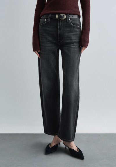 Zwarte jeans met wijde pijpen en een hoge taille, voorzien van witte stiksels en een zwarte riem. Gecombineerd met een bordeauxrode gebreide trui met structuur.