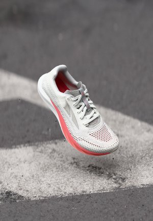 Chaussure de course légère en maille blanche avec un motif texturé, dotée d'une semelle rose, d'accents gris et d'un système de laçage traditionnel.