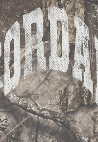 Tarnstoff mit weißer, fetter Schrift, die "JORDAN" schreibt, mit strukturierten Akzenten und einem natürlichen, erdigen Design.