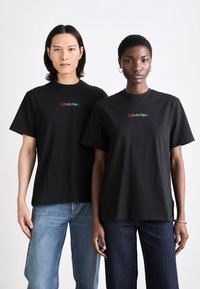 Juodi medvilniniai marškinėliai su spalvingu "Calvin Klein" logotipu krūtinėje, pritaikyti su trumpomis rankovėmis ir apvaliu iškirpimu.