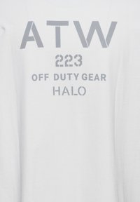 Weißer Stoff mit grauem Text "ATW 223 OFF DUTY GEAR HALO", in vier Zeilen vertikal zentriert angeordnet.