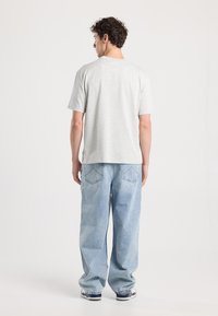 Light gray short-sleeve t-shirt paired with loose-fitting light blue jeans. The jeans have a classic five-pocket design and visible stitching.