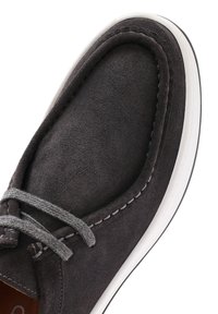 Zapato de ante gris oscuro con una textura suave, que presenta cordones grises y una suela de goma blanca. Acabados en costura a lo largo del borde.