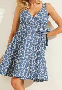 Blå mönstrad klänning med omslagdesign, som har vit blommig broderi, breda axelband och en knytning i midjan. Slät tygtextur.