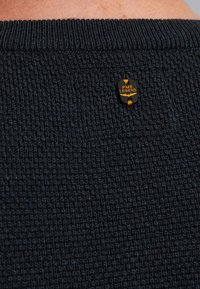 Donkerblauwe gebreide trui met een gestructureerd patroon, voorzien van een klein zwart label met "PME LEGEND" in gouden letters op de achterkant.