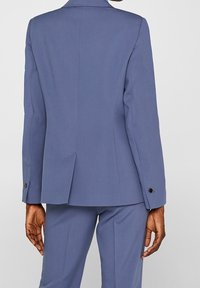 Skräddarsydd blå kavaj med en strukturerad design, enkel slits och knappaccent på ärmarna, tillverkad av ett slätt tyg.