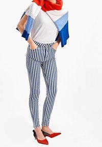 Randiga jeans i blått och vitt, figurnära design. Kombination med en vit skjorta och en flerfärgad stickad sjal; röda spetsiga klackar med svarta detaljer.