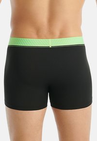 Černé plavkové šortky se strukturovaným světle zeleným pasem, který obsahuje kontrastní tenkou černou linii, a s propracovaným střihem pro pohodlí.