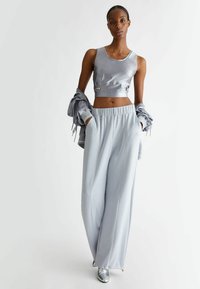 Top corto grigio chiaro con spalline e dettagli argento abbinato a pantaloni fluidi a vita alta con tasche laterali e cuciture a contrasto.