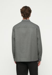 Sivá košeľa na zapínanie na gombíky s golierom, rovný strih, dlhé rukávy a jemná textúra. Má manžety so zapínaním na gombíky a detail s pásikom na chrbte.