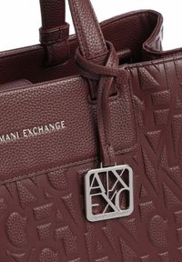 Bolso de piel marrón con una superficie texturizada y logotipo en relieve, acentos en hardware plateado y asas resistentes. Diseño elegante y estructurado.