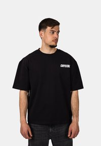 Černé bavlněné tričko s krátkým rukávem, na levé straně hrudi s bílým logem "CRYSTAL". Jednoduchý design, uvolněný střih.