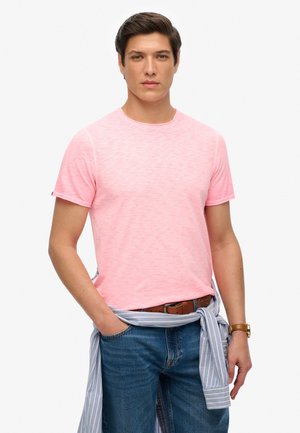 T-shirt rose clair à manches courtes en tissu doux, associé à un jean en denim bleu. Une chemise rayée bleu clair est nouée autour de la taille.