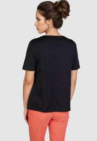 Schwarzes, kurzärmeliges T-Shirt aus Baumwolle, mit lockerer Passform und rundem Halsausschnitt, kombiniert mit bunt gefärbten Hosen.